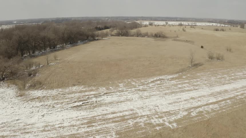 A slow aerial flyover of a desolate rural winter landscape showing dry fields and patches of snow