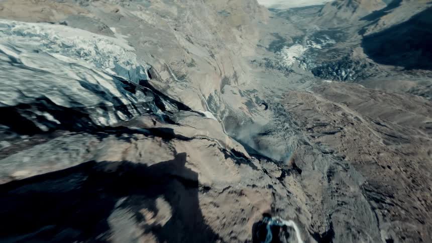 An exhilarating FPV drone flies over a massive glacier, diving steeply down its face and revealing cascading meltwater waterfalls