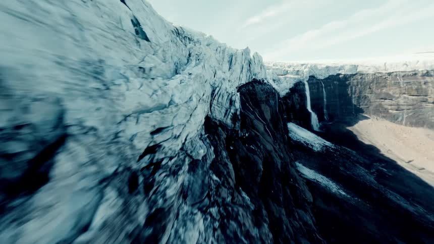 A fast-paced aerial flyover along the colossal edge of a melting glacier, revealing powerful waterfalls cascading down the steep rock cliffs
