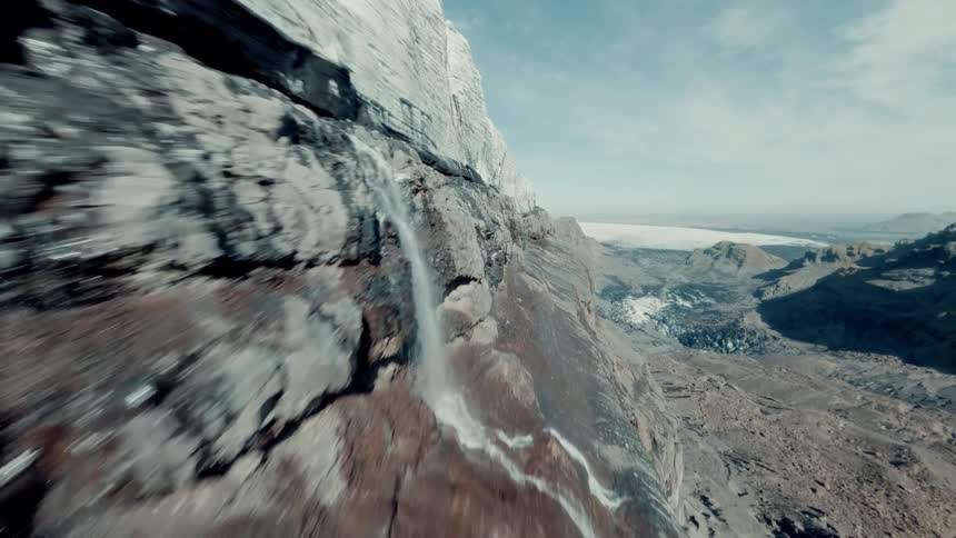 A thrilling FPV drone flight soars up a massive cliff face with waterfalls, revealing a vast glacier and surrounding valley