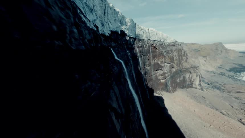 A fast-paced FPV drone flight along the edge of a colossal glacier, revealing meltwater waterfalls cascading down a dramatic cliff face