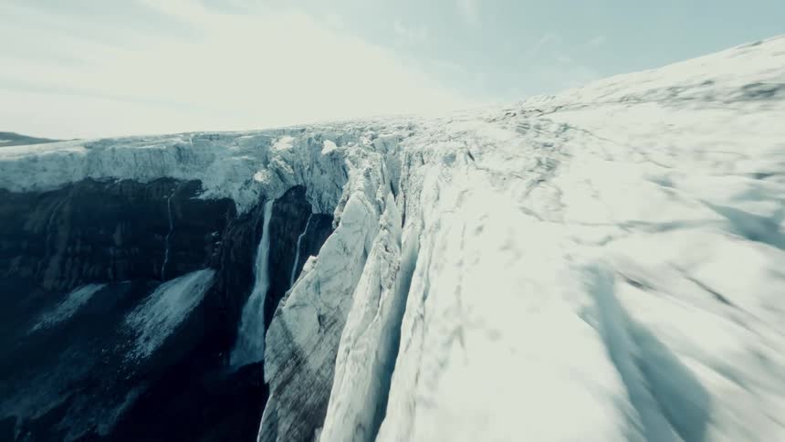 A thrilling FPV drone flight speeds along the icy wall of a massive glacier, revealing deep crevasses and a powerful melting waterfall
