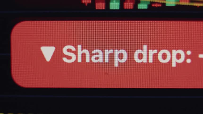 A macro shot of a financial chart on a screen displaying a red 'Sharp drop' notification indicating a market crash