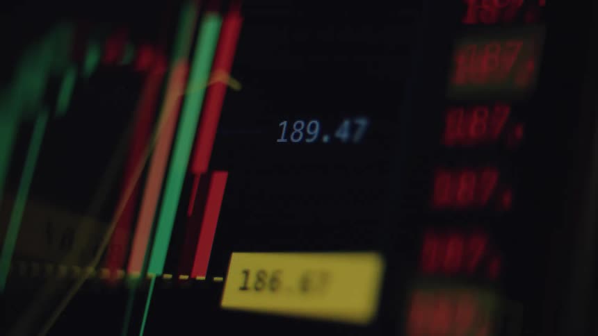 A close-up of a live stock market candlestick chart displays fluctuating financial data on a digital screen