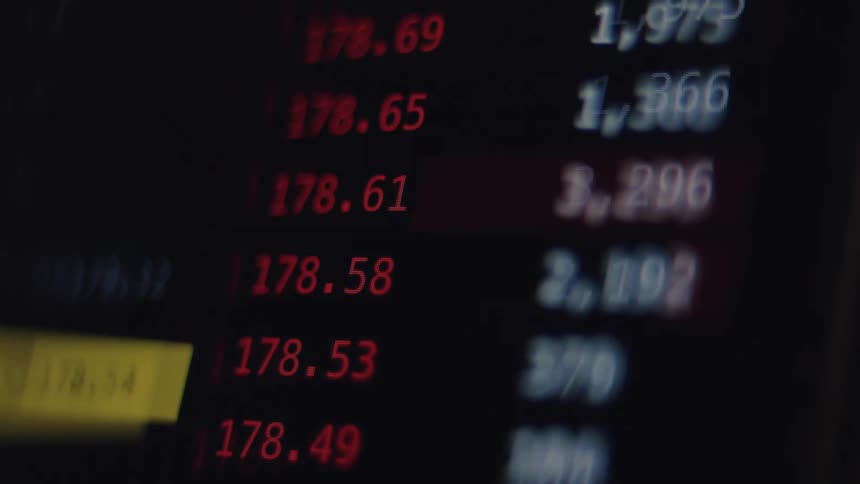 A close-up of a digital stock market ticker shows prices rapidly changing in red during a volatile trading session