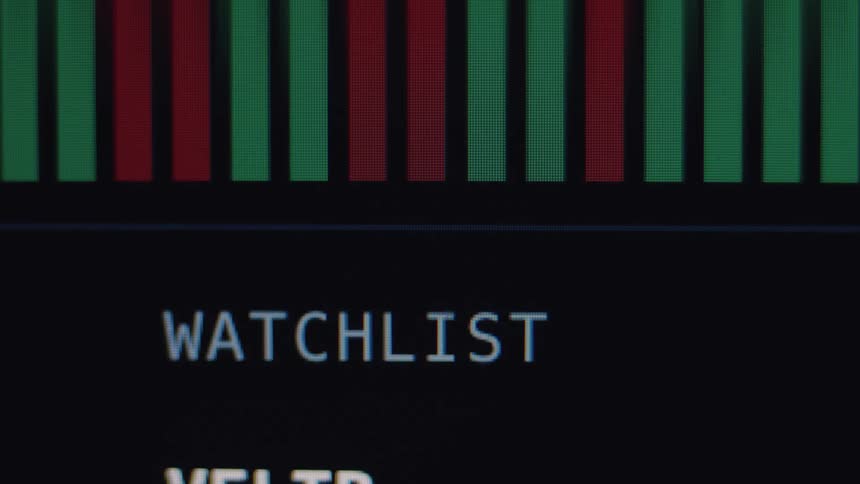 A close-up view of a stock market watchlist on a computer screen shows fluctuating green and red bars indicating gains and losses