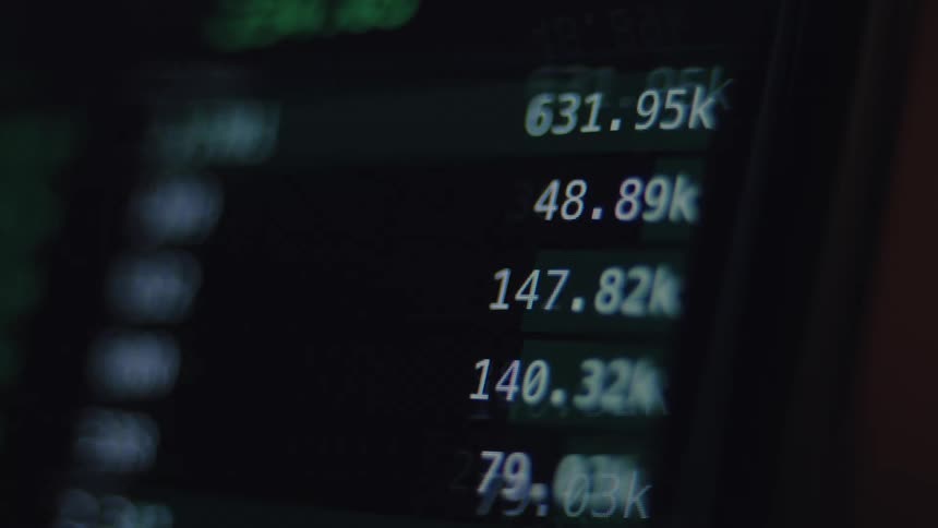 Rapidly changing digital financial data scrolls across a screen in a dark, abstract view