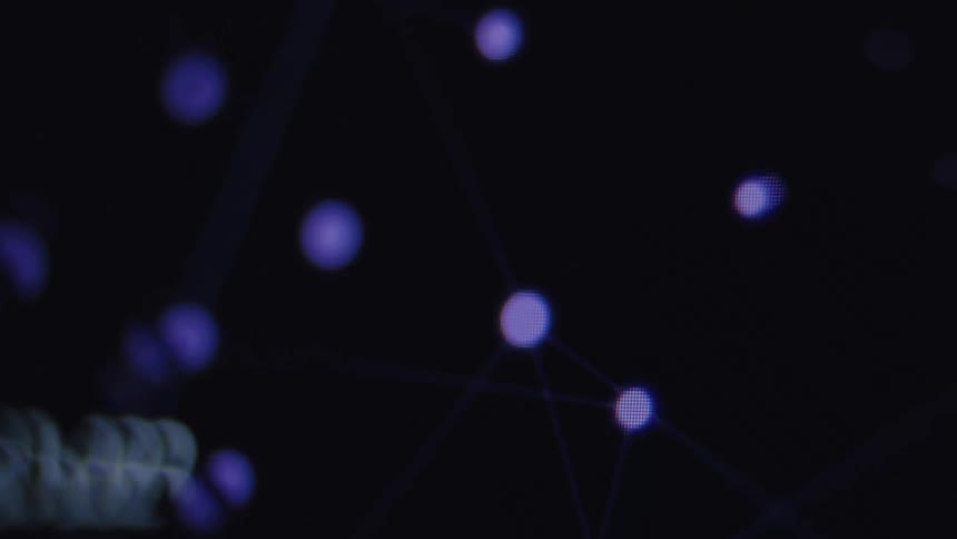 A close-up of a computer monitor shows a futuristic data visualization of a network structure with glowing nodes
