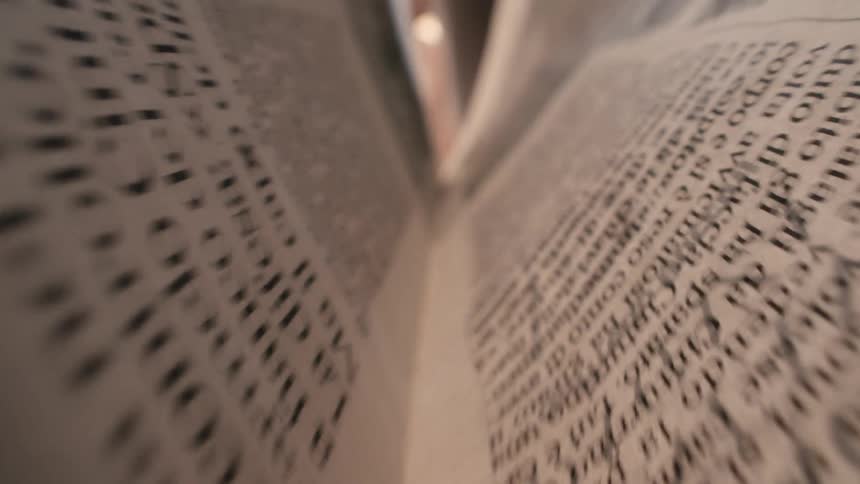 A dynamic extreme close-up shot pulls back from the blurred text between the pages of a newspaper