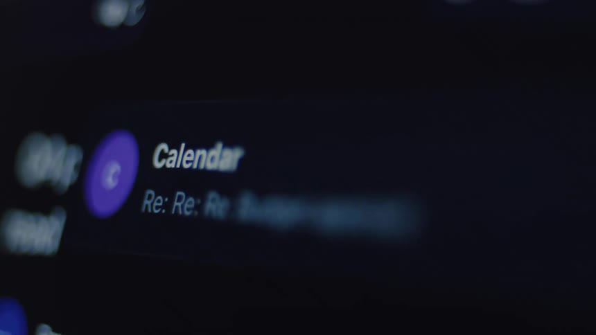 A close-up shot of a person scrolling through an email inbox on a screen with a dark mode interface
