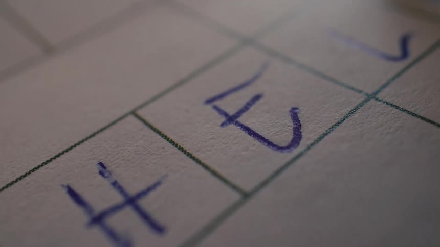 An extreme close-up shot of a blue ballpoint pen writing the word 'hell' on gridded paper