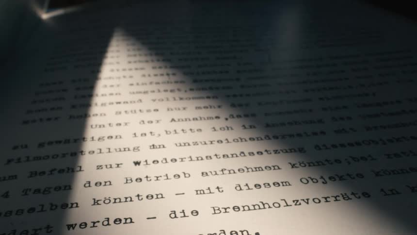 A beam of light slowly moves across a top-secret German document, revealing the typed text in a dark room