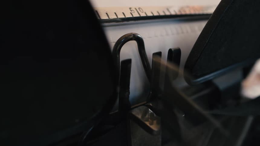 An extreme close-up shot shows the typebars of a vintage typewriter striking a piece of paper as words are written