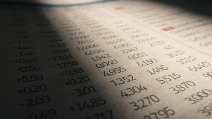 A beam of light scans across the stock market listings in a financial newspaper, highlighting the changing numbers