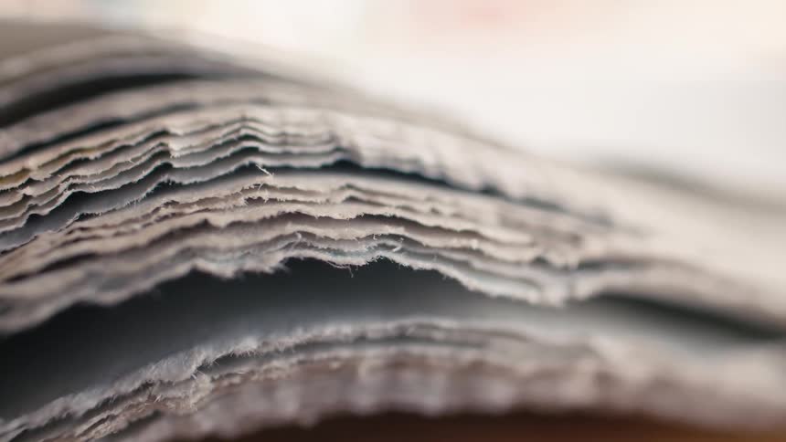 A pull focus macro shot reveals the textured, frayed edges of stacked newspaper pages