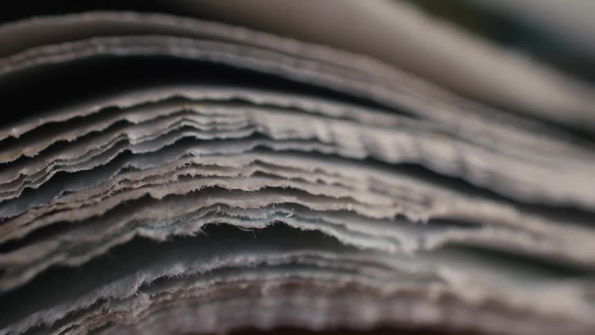 An intimate macro shot reveals the delicate, layered texture of old newspaper pages as a finger flips through them