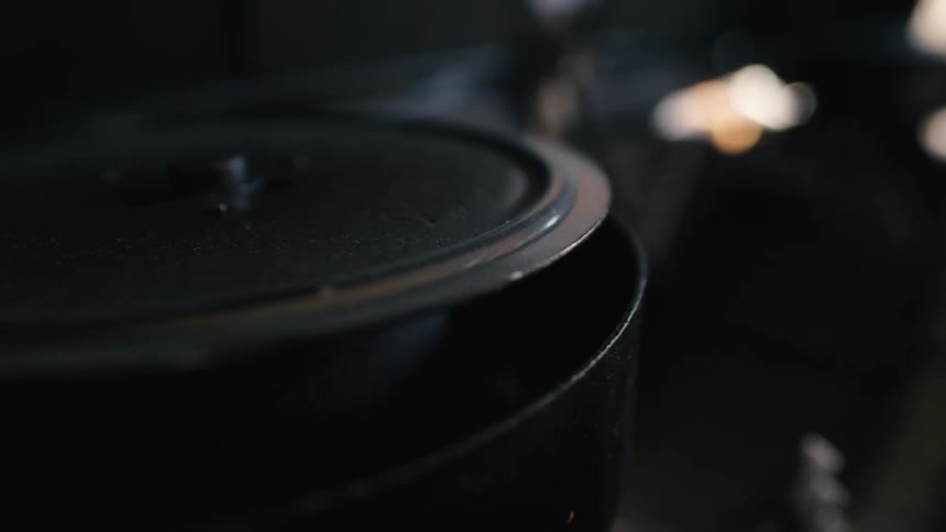 Close up of a black pot with the lid slightly ajar, steam rising from the simmering contents inside