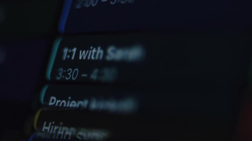 A close-up shot of a blurry digital calendar shows a busy schedule of meetings and appointments on a screen