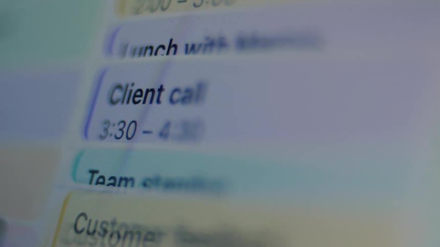 A close-up, out-of-focus view of appointments like 'Client call' being added to a digital calendar on a screen