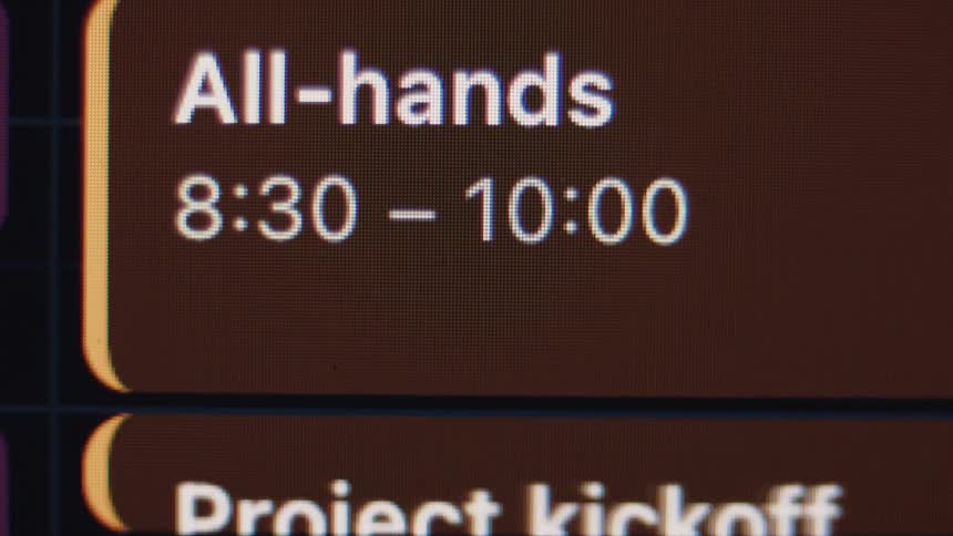 An extreme close-up shot of a digital calendar on a screen showing an 'All-hands' meeting scheduled for 8:30 to 10:00