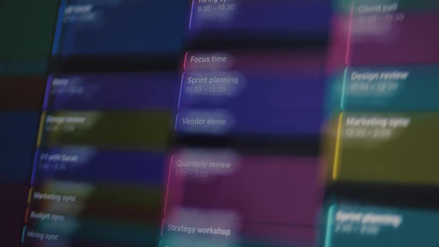 An abstract, shallow focus shot of a futuristic digital calendar filling up with glowing, colorful work meetings