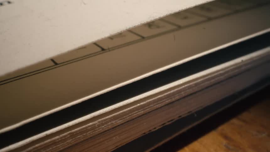 A close-up, macro shot shows the pages of an old, thick book with a moving shadow casting across them