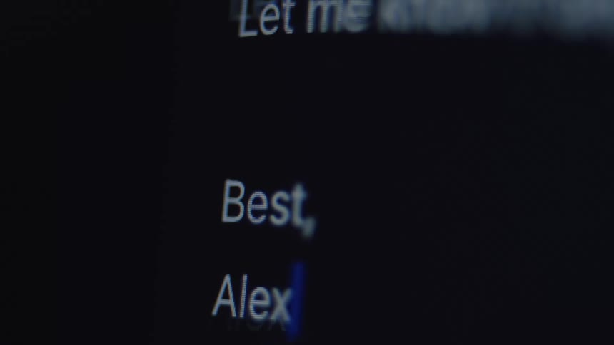 A macro shot of a person typing and then deleting the sign-off 'Best, Alex' on a dark computer screen
