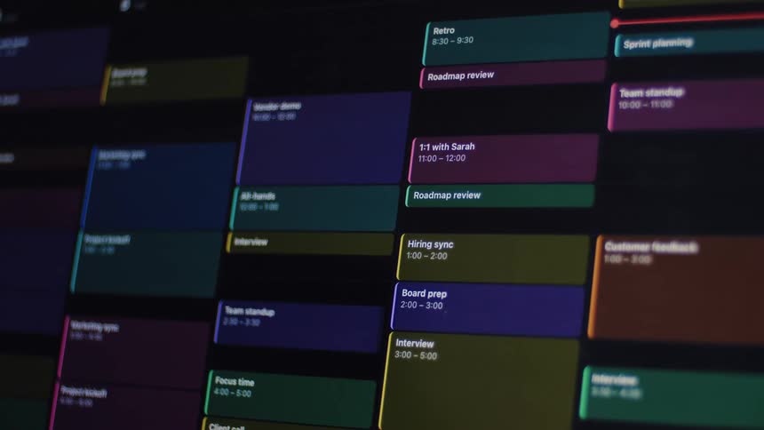 Close-up of a digital calendar in dark mode populating with a busy schedule of corporate meetings and appointments