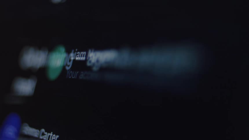 A close-up, out-of-focus view of a digital email inbox scrolling rapidly on a dark screen