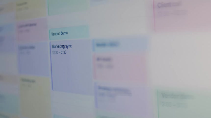 A close-up, angled view of a colorful digital calendar on a screen displaying a busy work schedule full of meetings and appointments