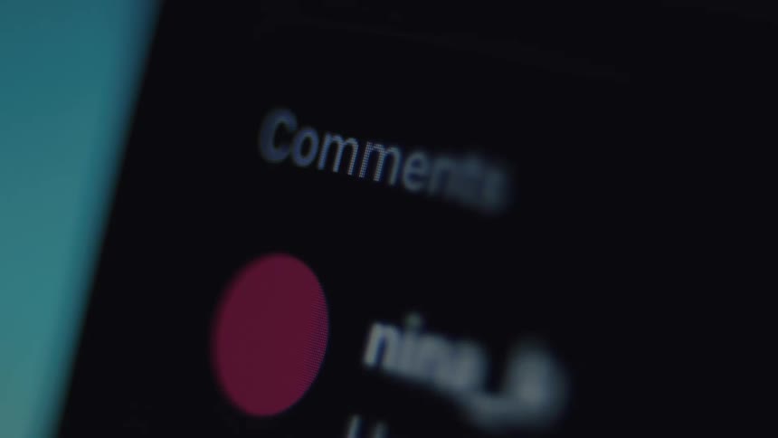 A macro close-up of a smartphone screen showing the comment section of a social media post with user profiles scrolling by in dark mode