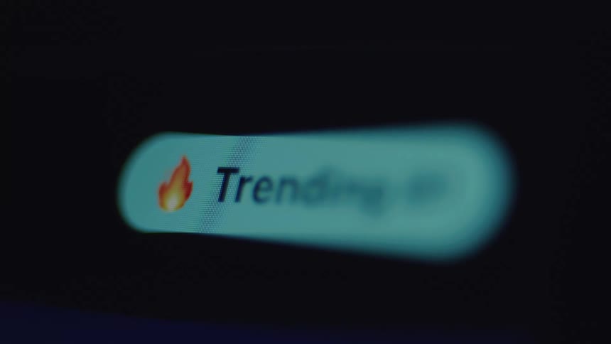 Macro shot of a 'Trending' button with a fire emoji on a digital screen, symbolizing online popularity