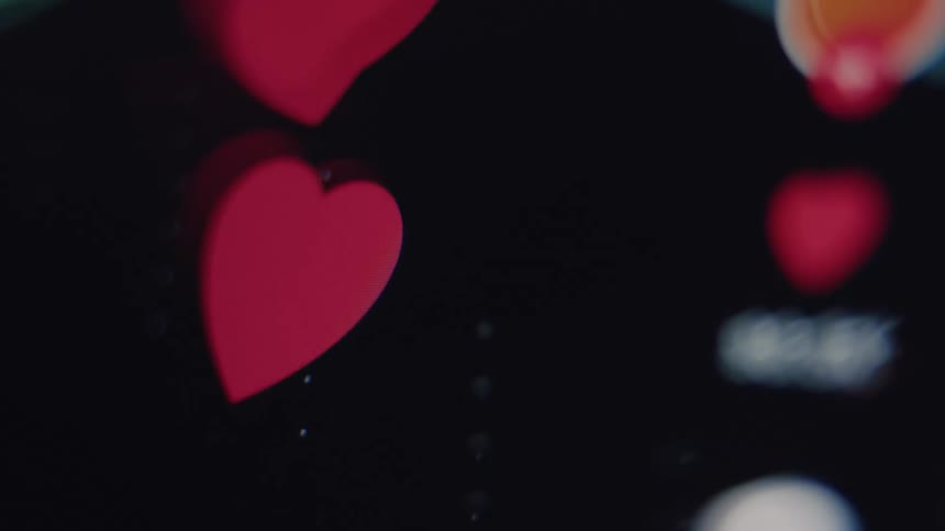 Macro, out-of-focus shot of animated red heart icons floating up on a social media live stream screen, representing likes and engagement