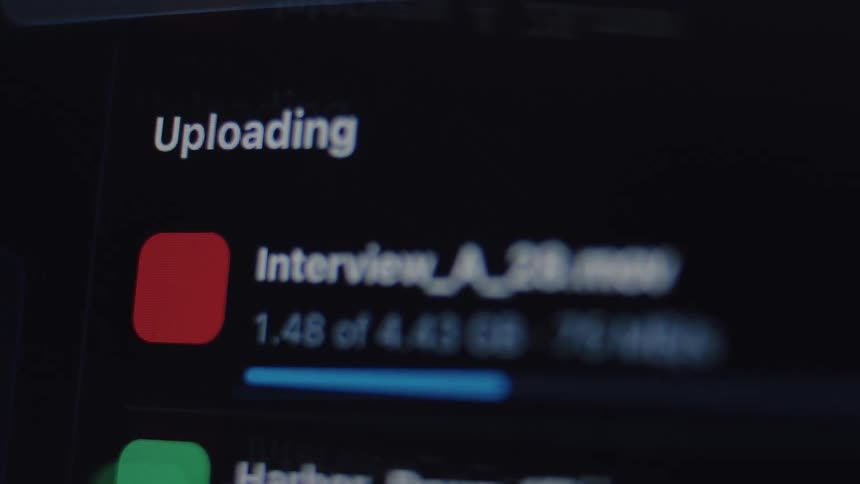 A macro shot of a computer screen displays a list of files with their progress bars as they are uploaded to a cloud service in dark mode