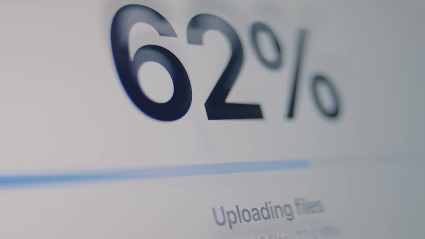 A close-up of a computer screen shows a file upload progress bar with a percentage counter quickly reaching completion