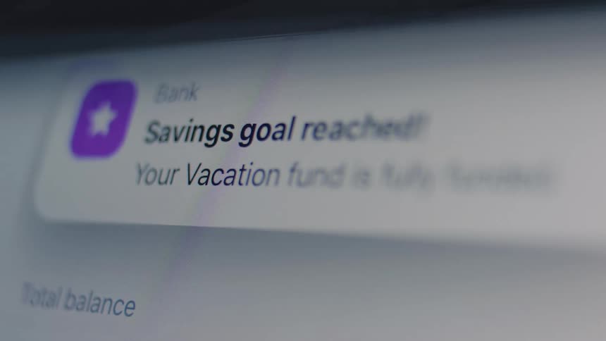 A close-up of a banking app notification on a digital screen stating that a vacation savings goal has been reached