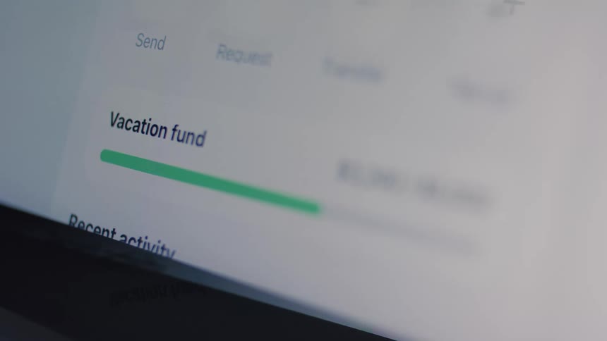 A close-up shot of a digital banking app shows the progress of a growing vacation fund on a computer screen