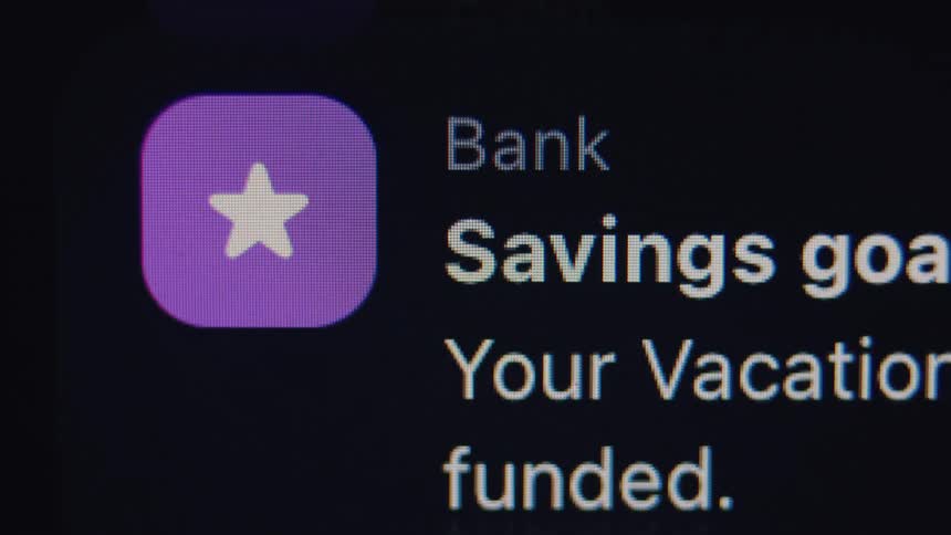 A close-up shot of a banking app notification on a smartphone screen showing a vacation savings goal has been successfully funded