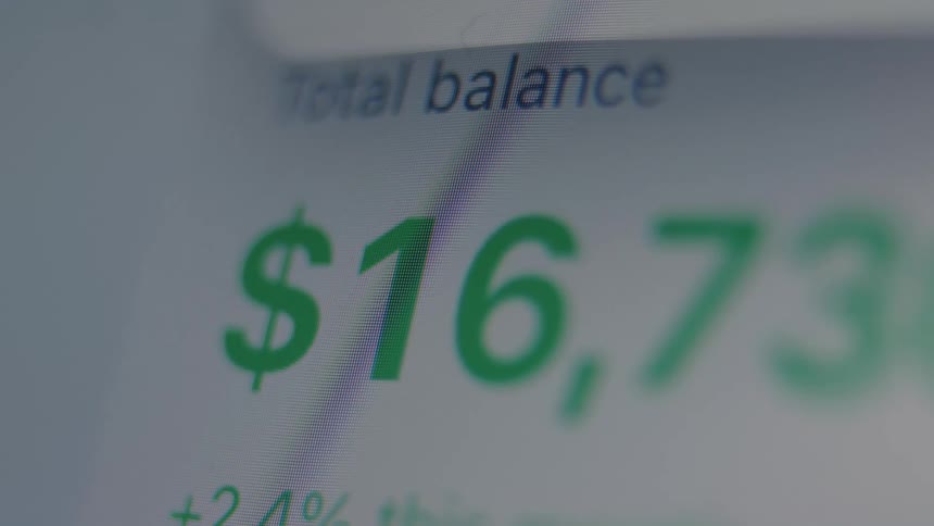 A close-up view of a digital screen shows the total balance of an investment account rapidly increasing in value