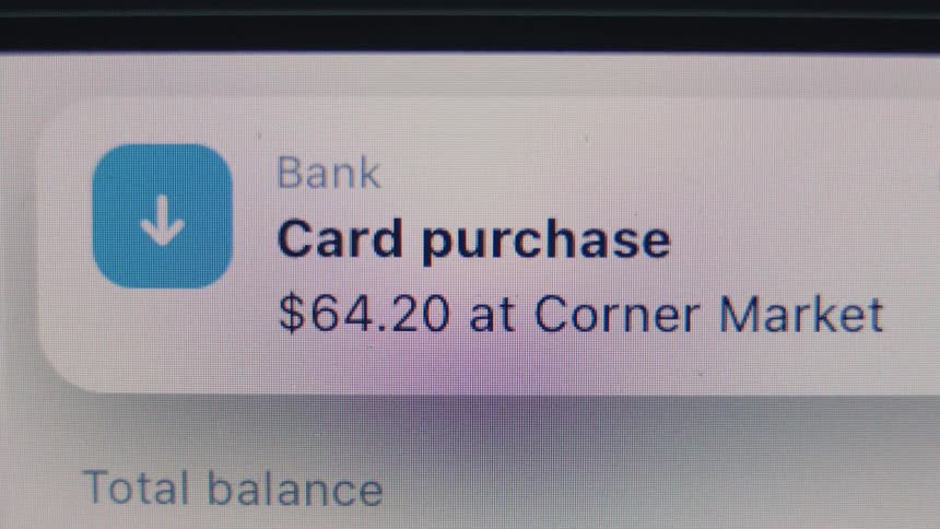 A close-up of a smartphone screen shows a bank notification for a recent card purchase at a corner market