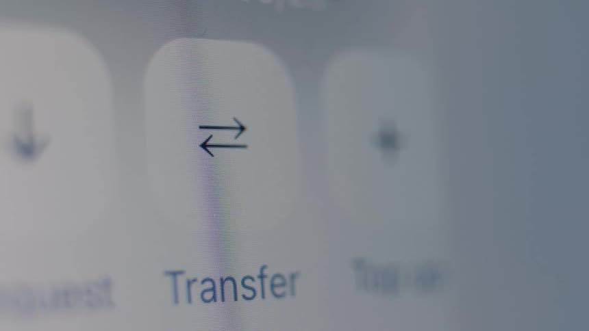 A macro shot of a finger tapping the 'Transfer' button on a digital screen, initiating a transaction in an online banking app