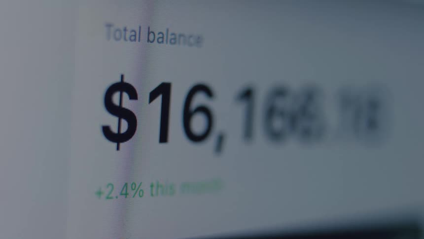 A close-up shot of a computer screen shows a rapidly decreasing financial balance on an online banking or investment website