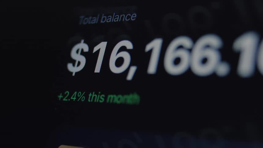 A close-up shot shows a digital investment portfolio's total balance rapidly fluctuating on a dark screen