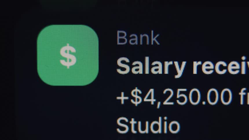 A close-up of a digital screen shows a notification for a salary payment of over four thousand dollars from a banking app