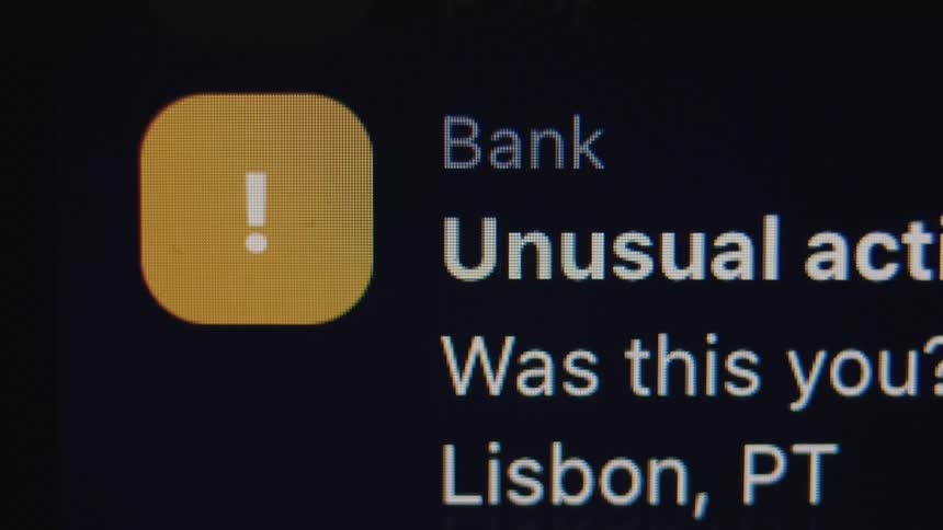 A close-up shot of a smartphone screen displaying a flashing, glitchy bank notification for unusual activity in Lisbon, Portugal