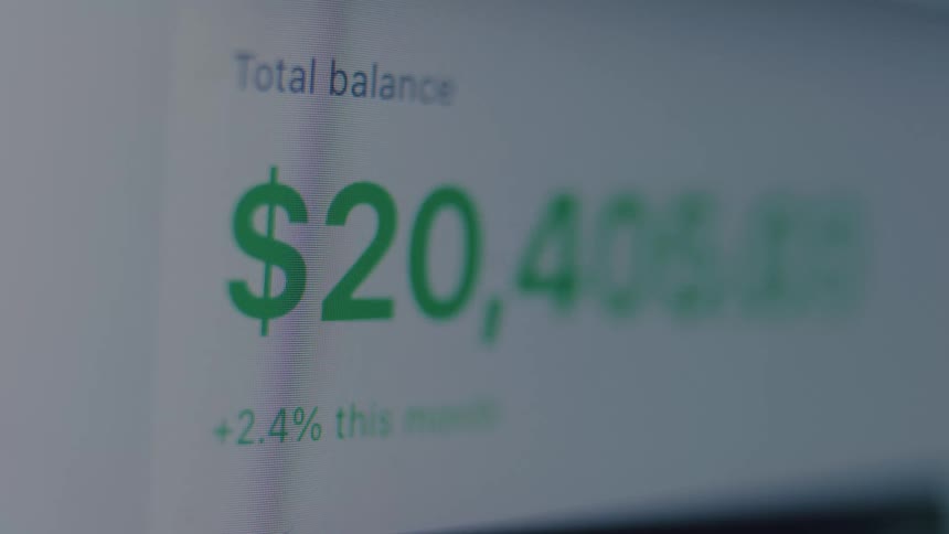 A close-up of a digital screen shows a financial account's total balance rapidly increasing, symbolizing wealth and investment growth