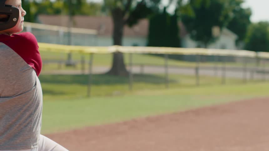 Slow motion close-up of a young baseball player hitting the ball with a bat on a sunny day