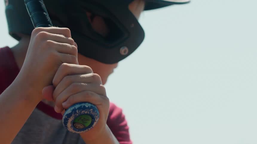 Close-up of a young little league player's hands gripping a baseball bat tightly while wearing a helmet