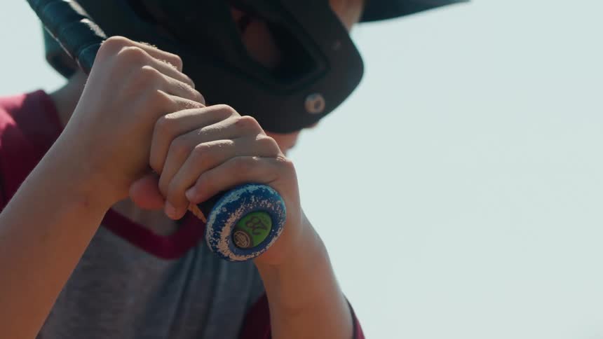 A young baseball player wearing a helmet grips a bat tightly in slow motion, focused and ready to swing