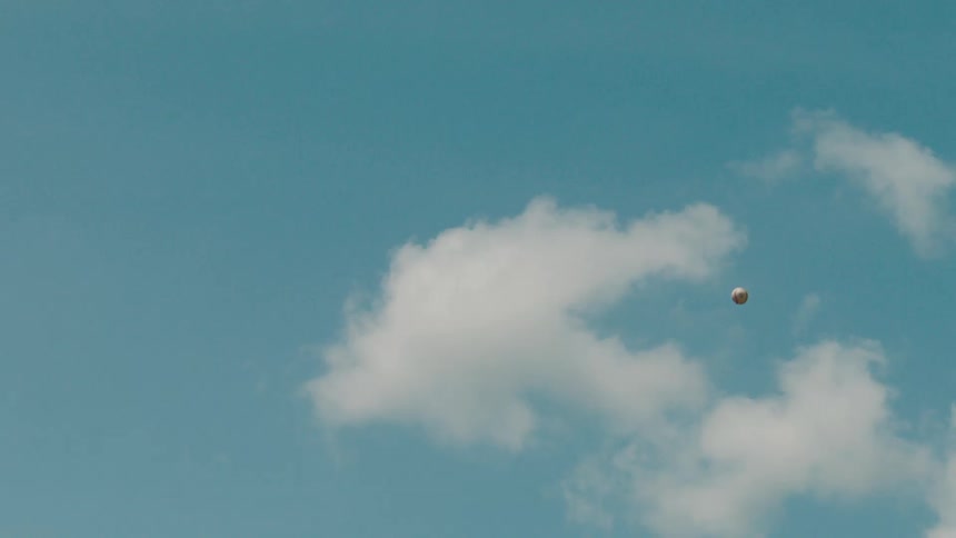A baseball soars through the cloudy blue sky and falls back down in slow motion